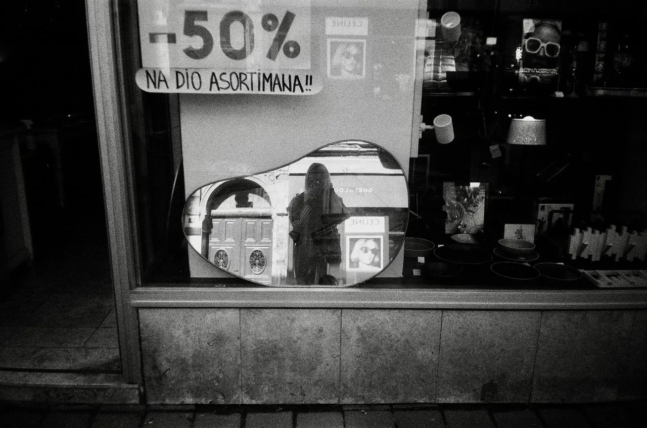 A reflective black and white photo of a shop window with a person in the mirror, offering -50% sale.