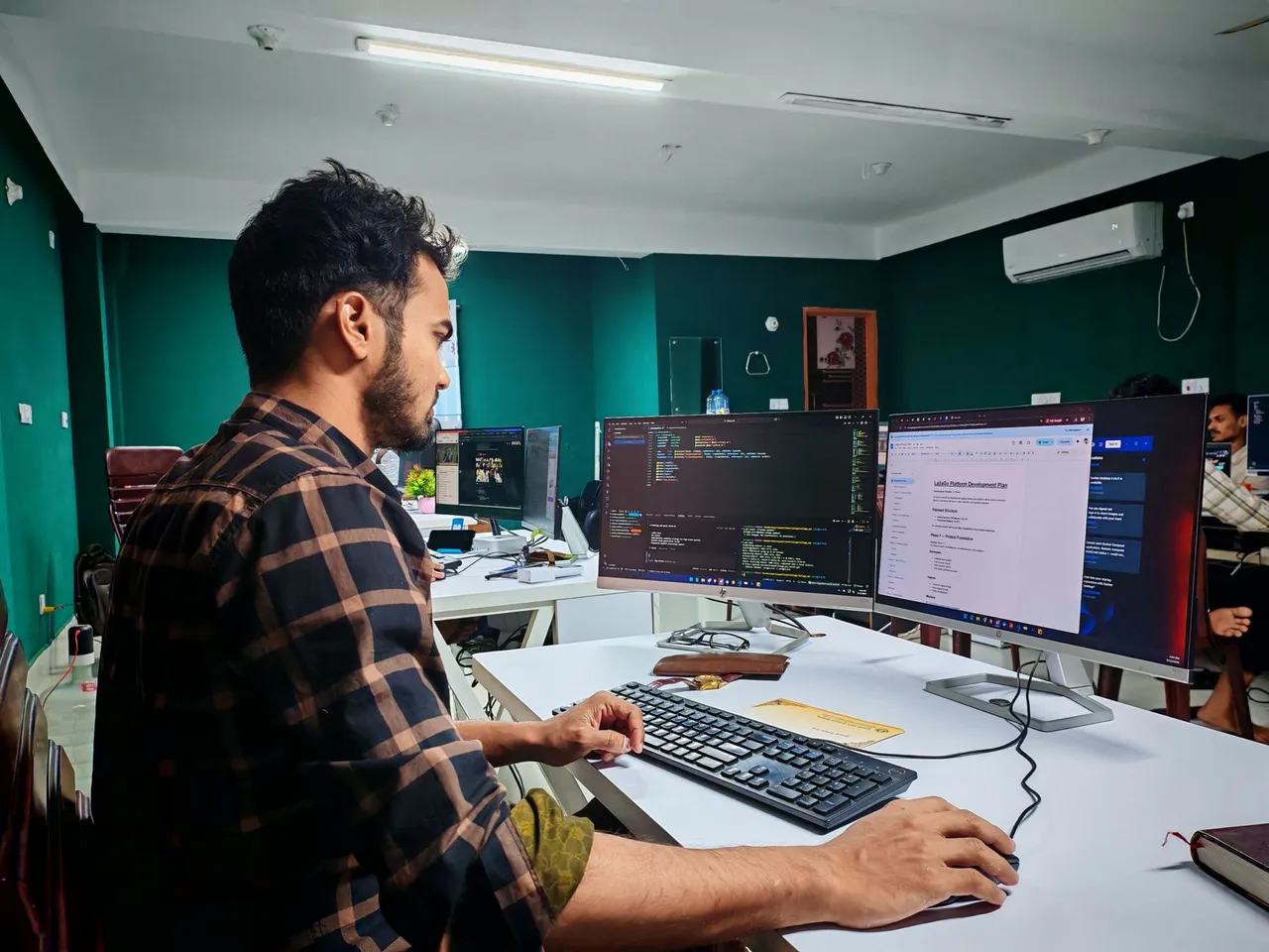 A programmer with headphones focuses on coding at a computer setup with dual monitors.
