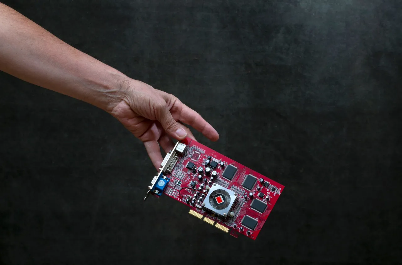 A close-up of a hand holding a red graphics card against a dark textured background.