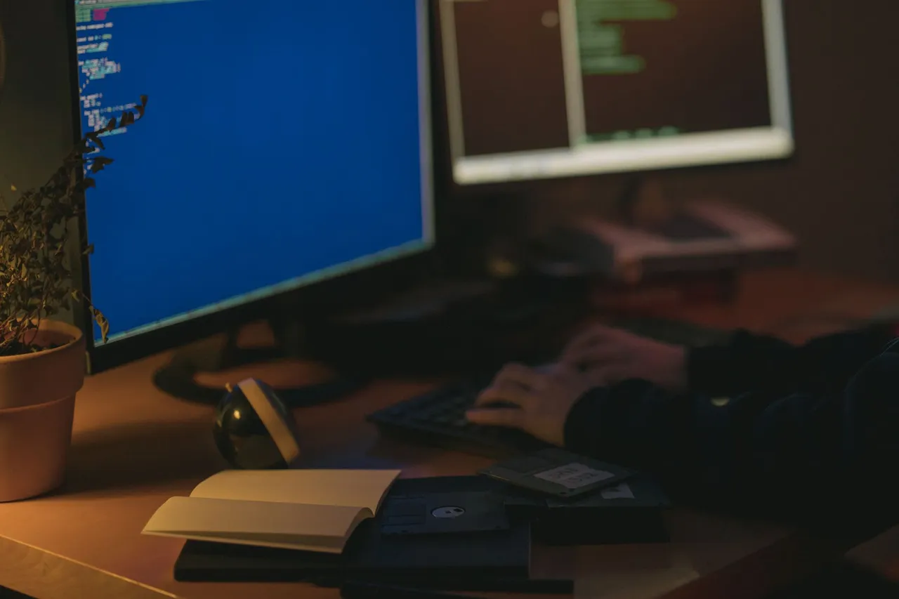 Individual programming in a dimly lit room with dual monitors.