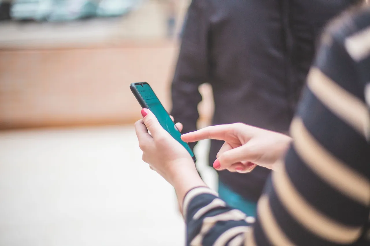 Close-up of a person's hand using a smartphone outdoors on a bright day.
