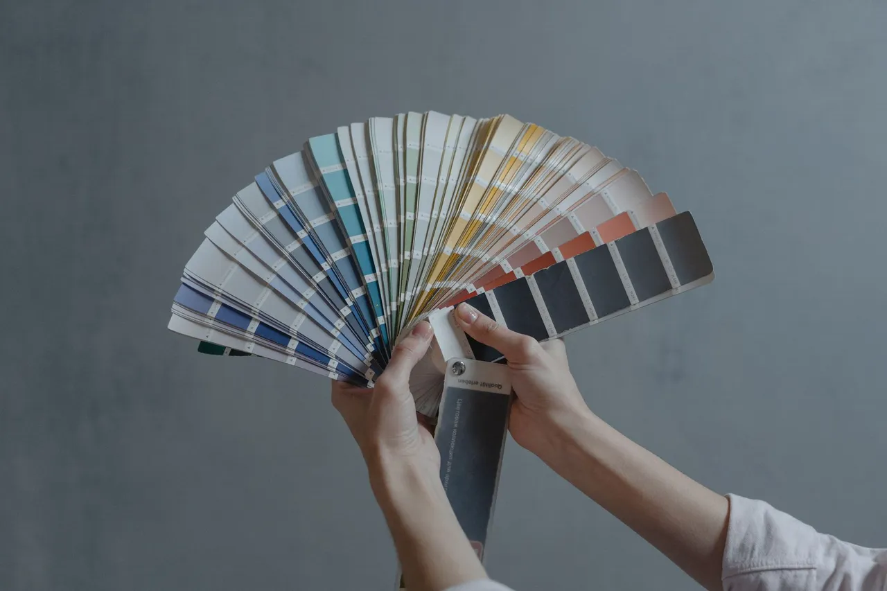 Hands holding a colorful fan of swatches on a gray backdrop, ideal for design themes.