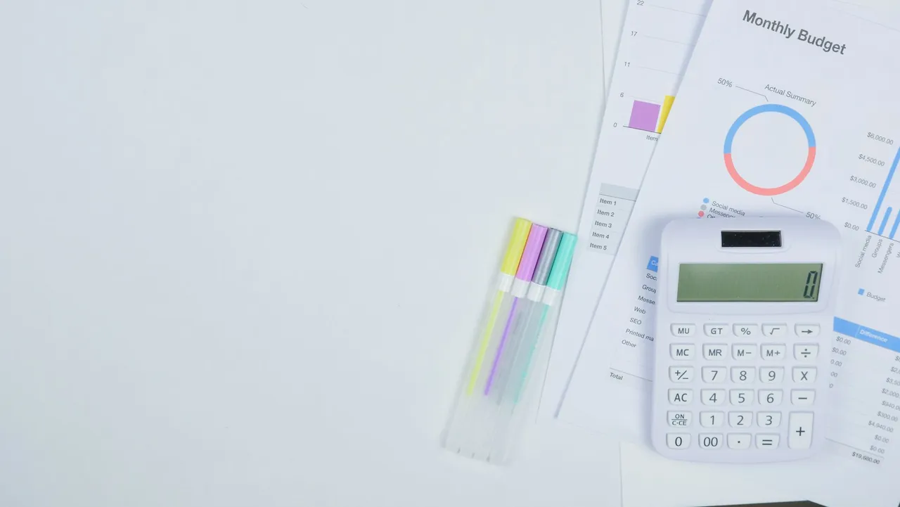 Minimalist office desk with a calculator, budget planning documents, and colorful pens.