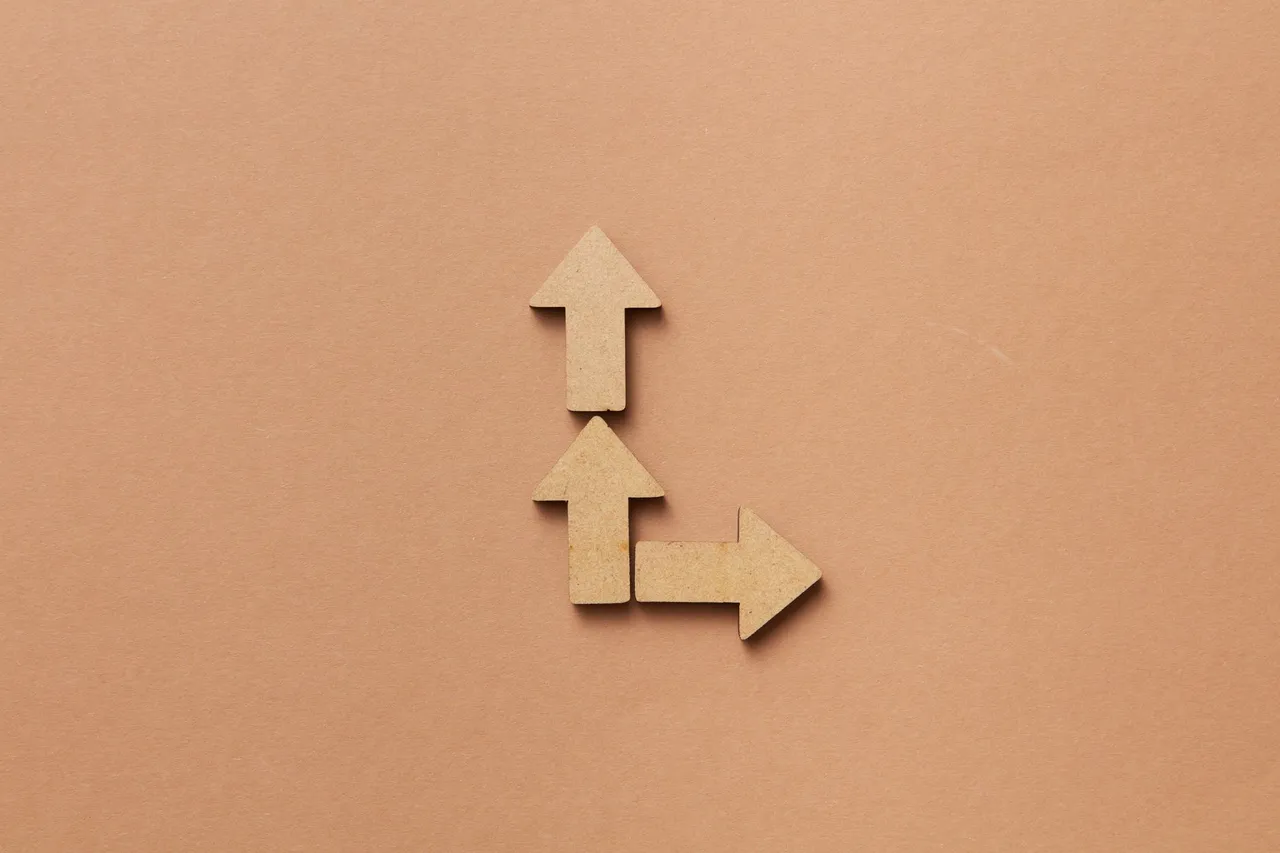 Three cardboard arrows arranged on a brown background, symbolizing direction and choice.