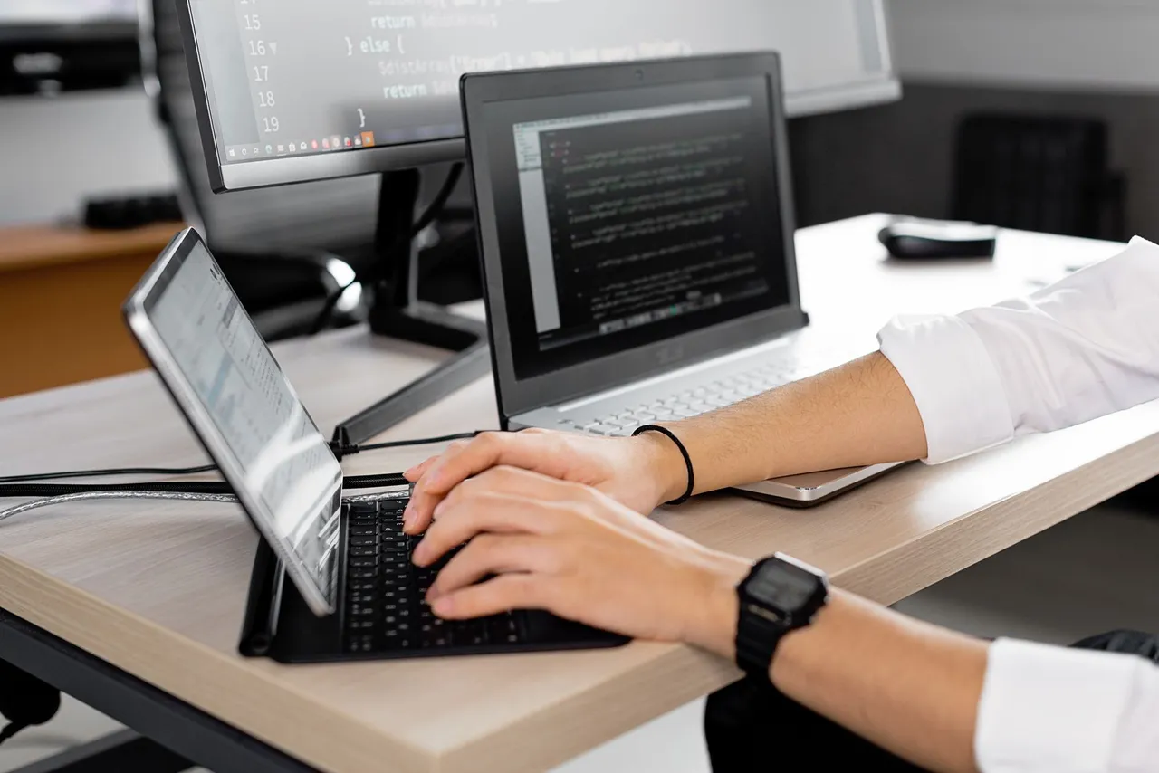 Candid shot of a programmer at work using multiple screens to code in a modern office.